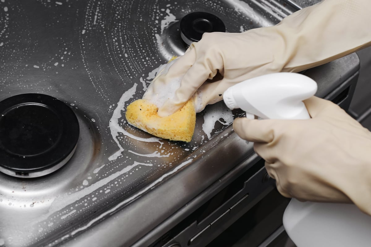 Kitchen hygiene routine at home. Wiping cooktop during regular household cleaning process.